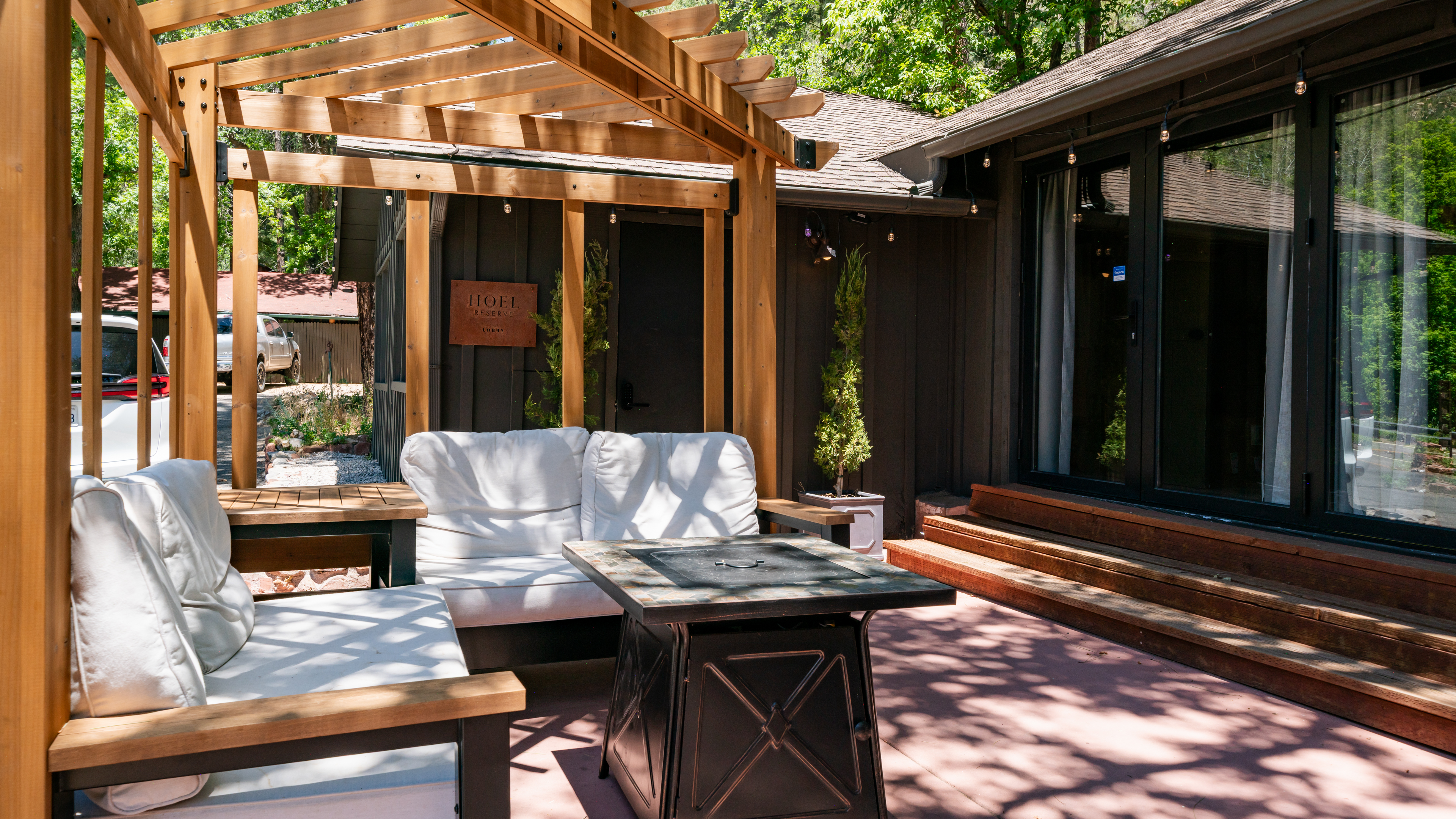 A cozy outdoor seating area with a wood pergola, white cushioned furniture, and a coffee table.